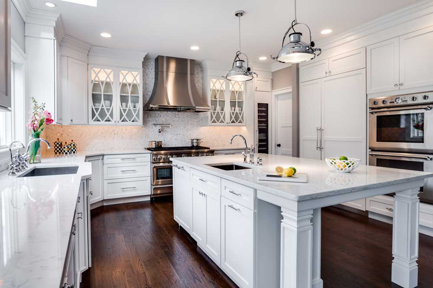 White kitchen with vinyl wood flooring. Kitchen with chrome pendant lights over white kitchen island with marble countertop