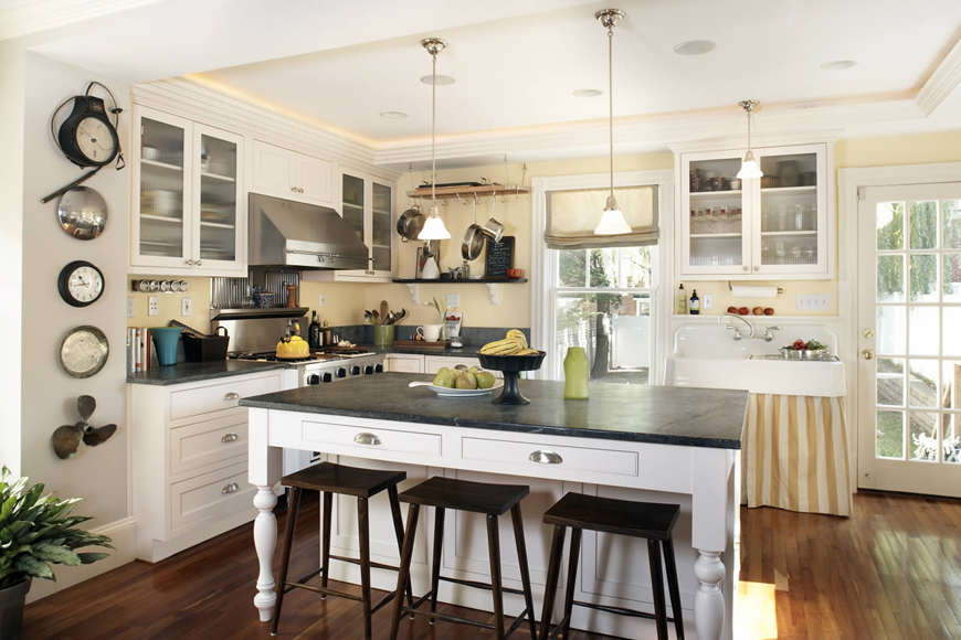 White kitchen with saddle bar stools. Kitchen with mini pendant lights over white kitchen island with black countertops